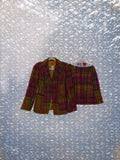 Plaid suit jacket and skirt set on hangers against a textured blue background